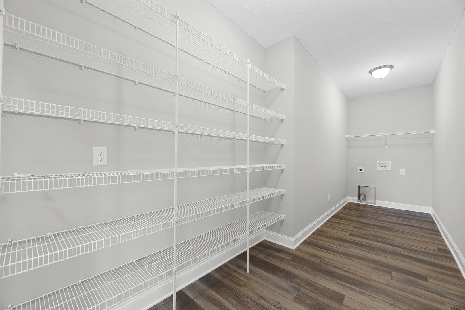 White built-in shelves along a plaster wall, hardwood flooring with white baseboard trim, recessed ceiling light, silver trash can set into shelving, and white electrical outlet