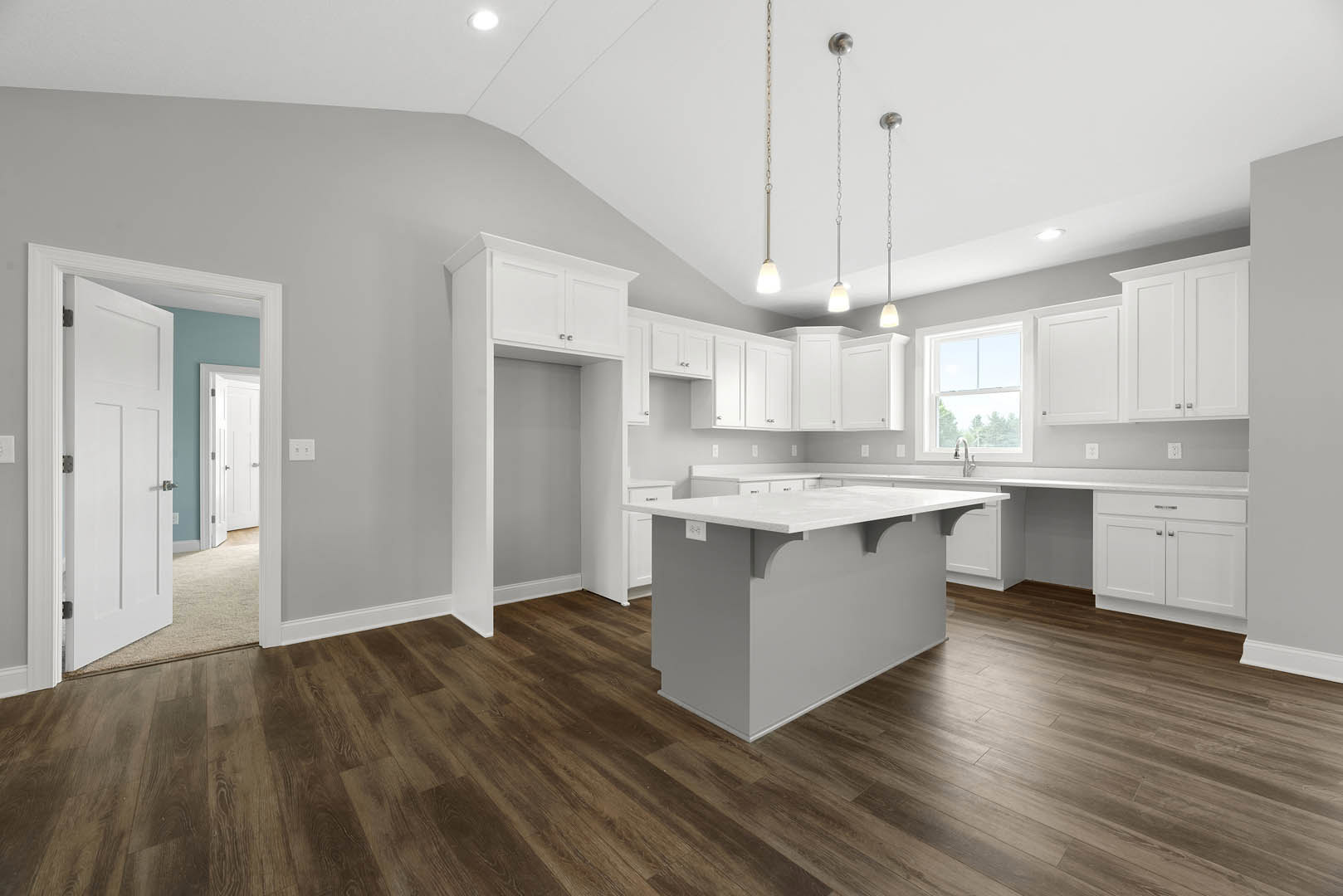 White kitchen cabinets, light hardwood flooring, marble countertop, stainless steel sink, silver cabinet handles, white walls, recessed ceiling lights, large window with person