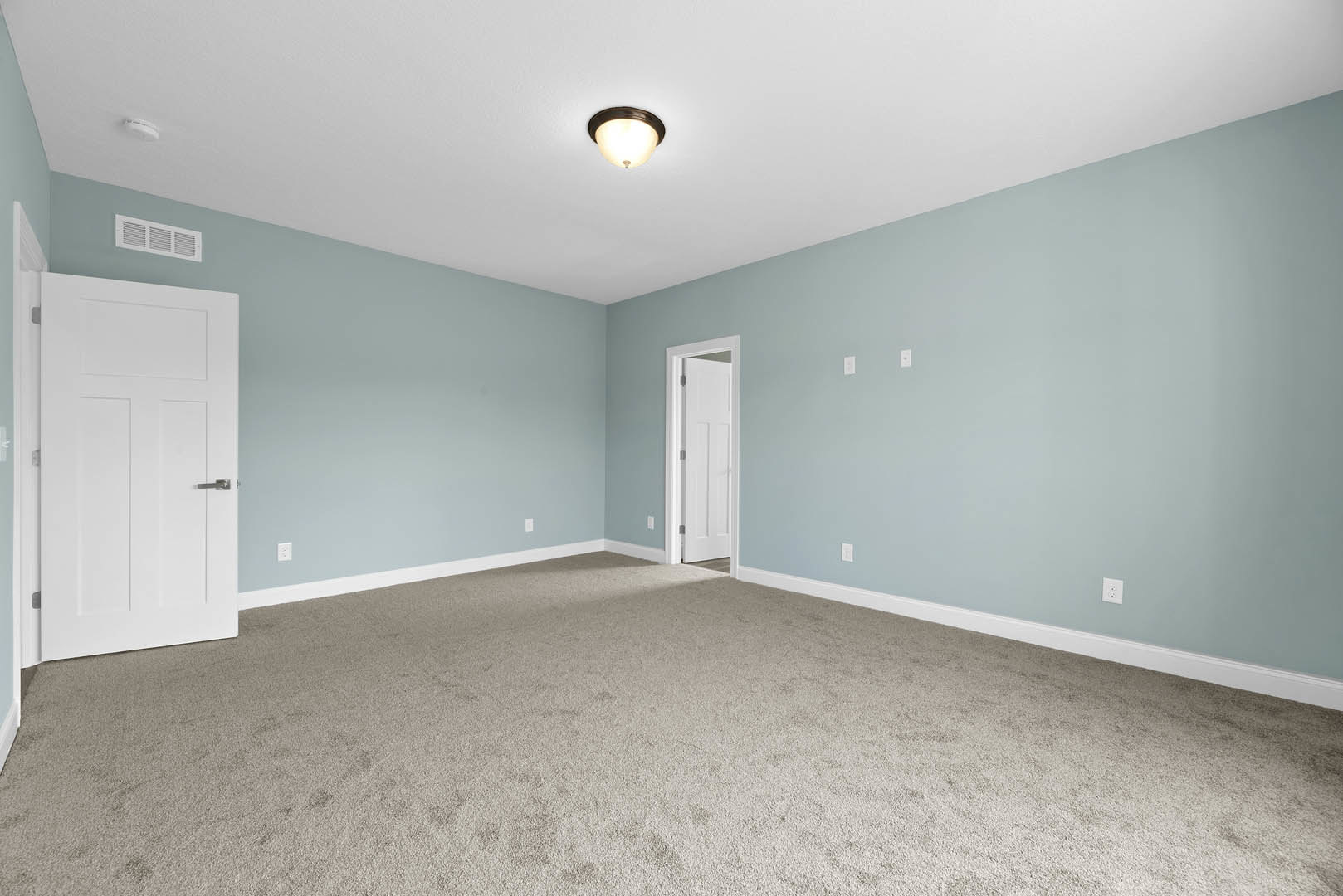 Carpeted room with light blue walls, white door featuring silver handle, second white door with round doorknob, ceiling-mounted light fixture, wall vent