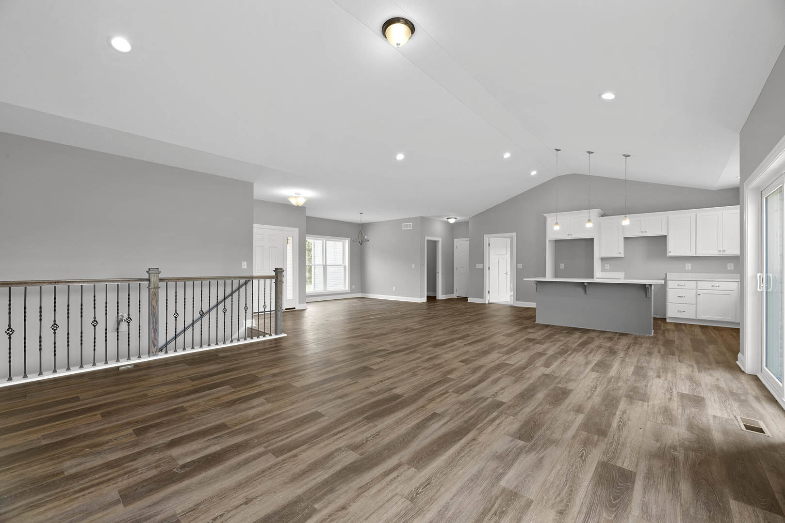 Spacious room with wood laminate flooring, metal staircase railing, plaster walls, ceiling light fixture, and window with closed blinds