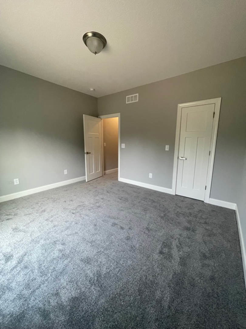 Carpeted room with white walls, white door featuring a silver handle, ceiling fan, and light switch visible near the door.