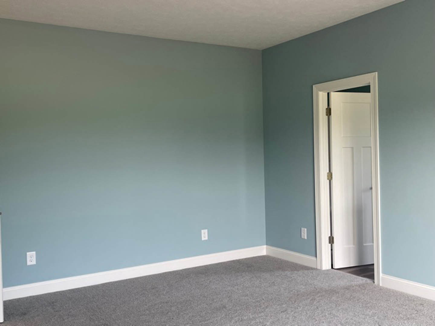 White paneled door with gold hinge open to a room featuring blue walls, white ceiling molding, beige carpet flooring, and a wooden table in the foreground.