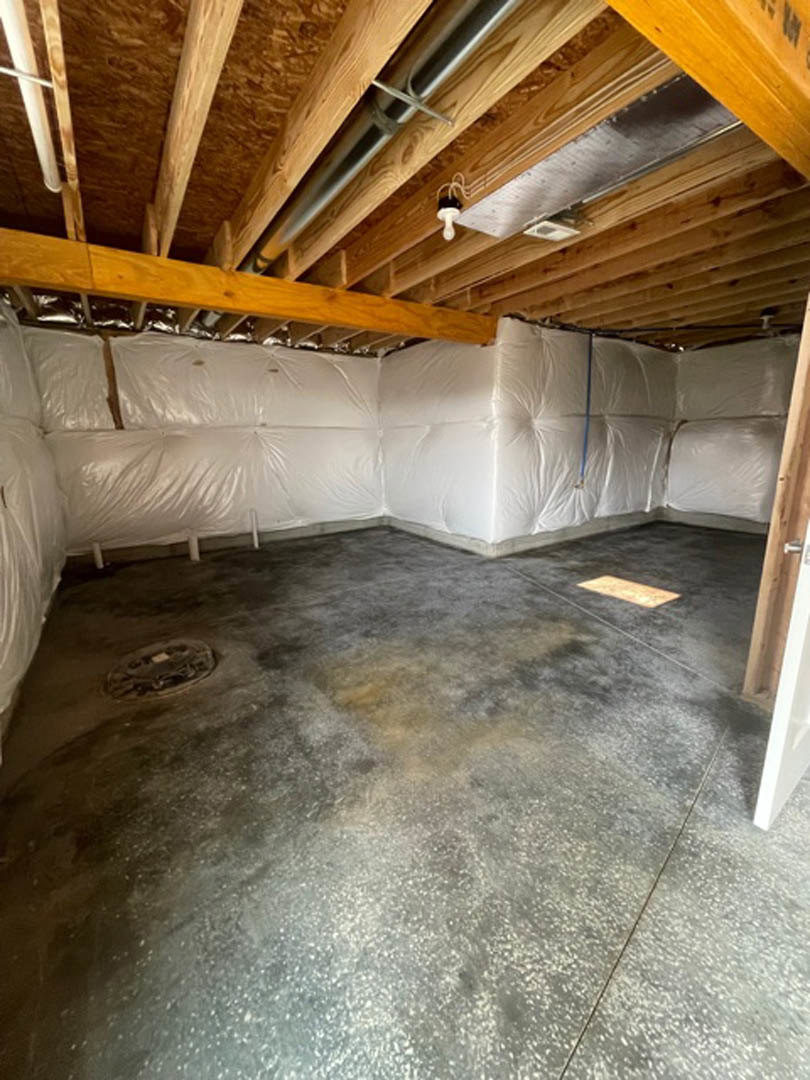 Unfinished room with concrete floor covered by white plastic, exposed wooden ceiling beams, and visible metal pipes