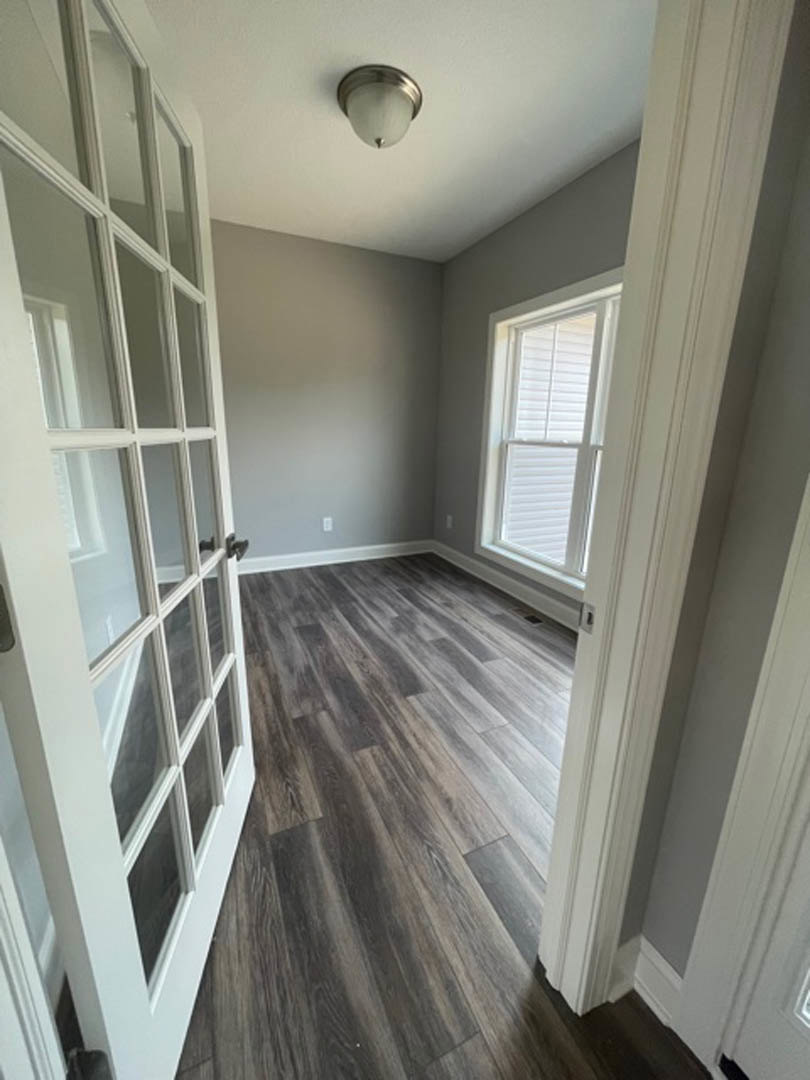Wood floor room with white door, ceiling light fixture, and window with closed blinds