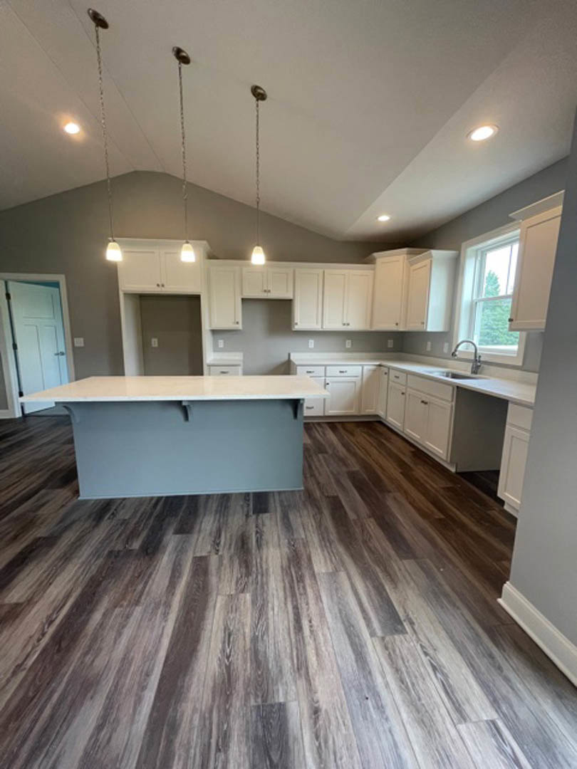 Spacious kitchen featuring a large central island with light-colored countertop, white cabinetry, laminate flooring, tiled backsplash, and a window with a white frame.
