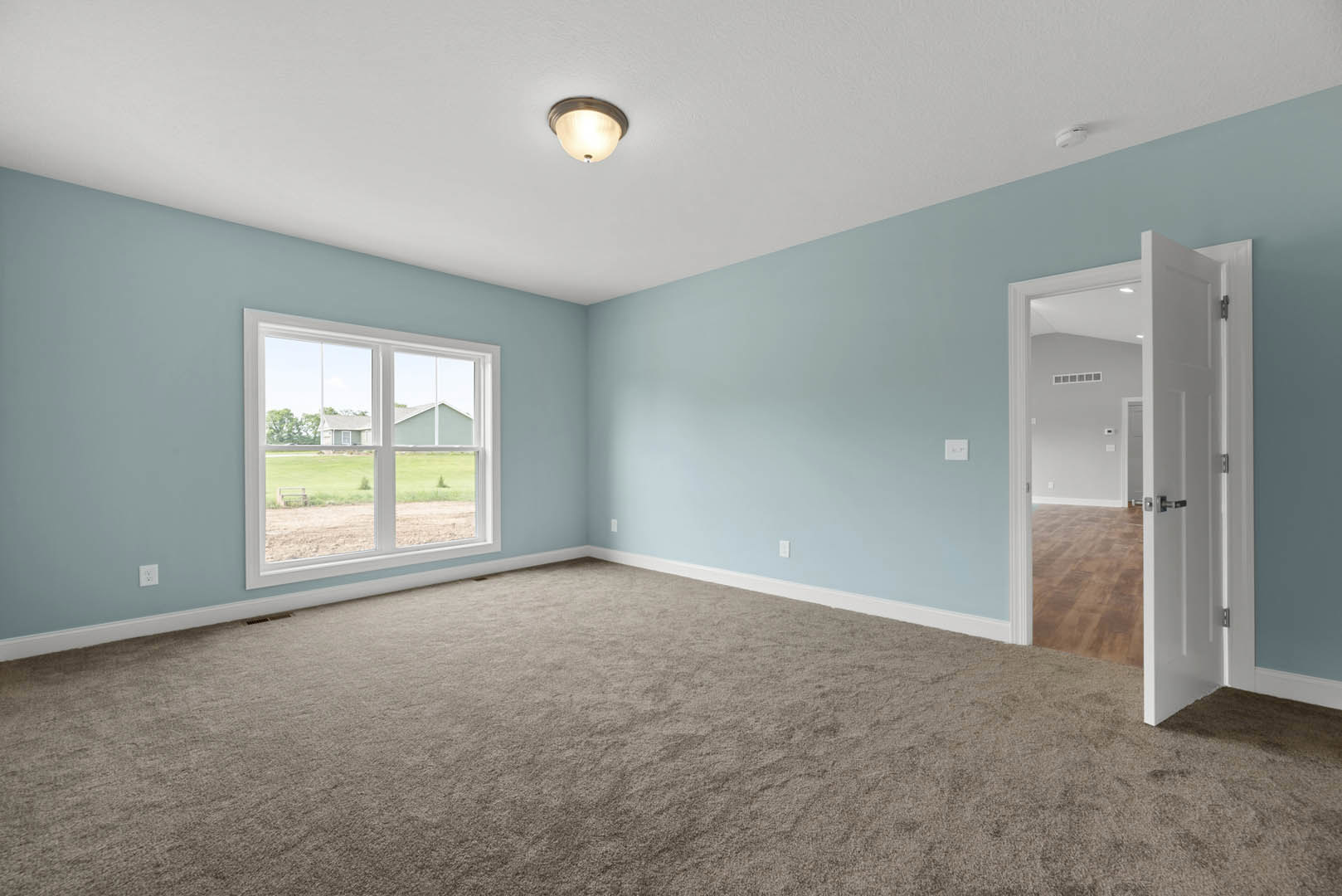 Carpeted room with light blue walls, white open door, ceiling light fixture, and window overlooking neighboring house