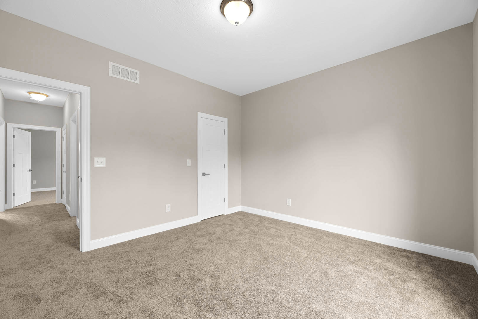 Carpeted room with white paneled door featuring a silver handle, white walls, ceiling light fixture, wall vent, and crown molding.