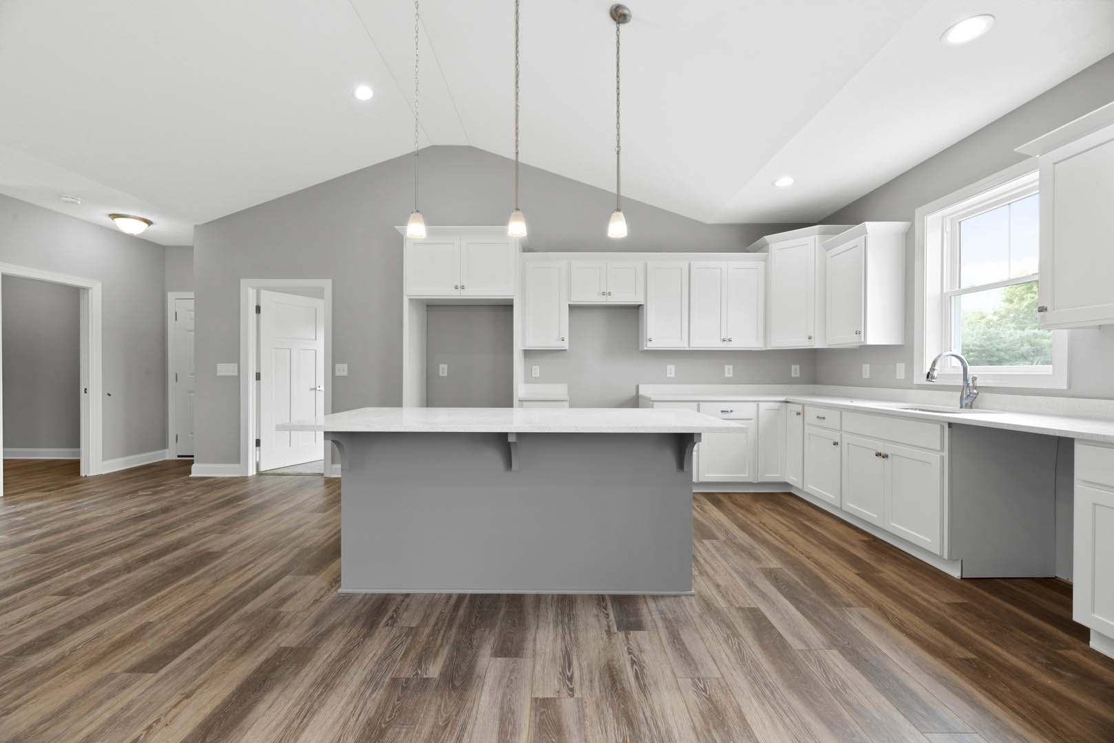 White kitchen cabinets, central island with stone countertop, wood flooring, grey accent wall, recessed ceiling lighting, white door with silver handles