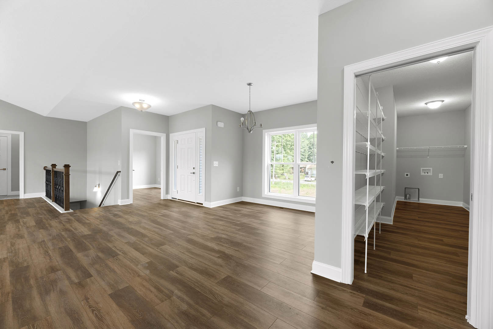 Room with wood flooring, white door with silver handle, white shelves, ceiling light fixture, window overlooking street and trees, close-up of wooden shelf