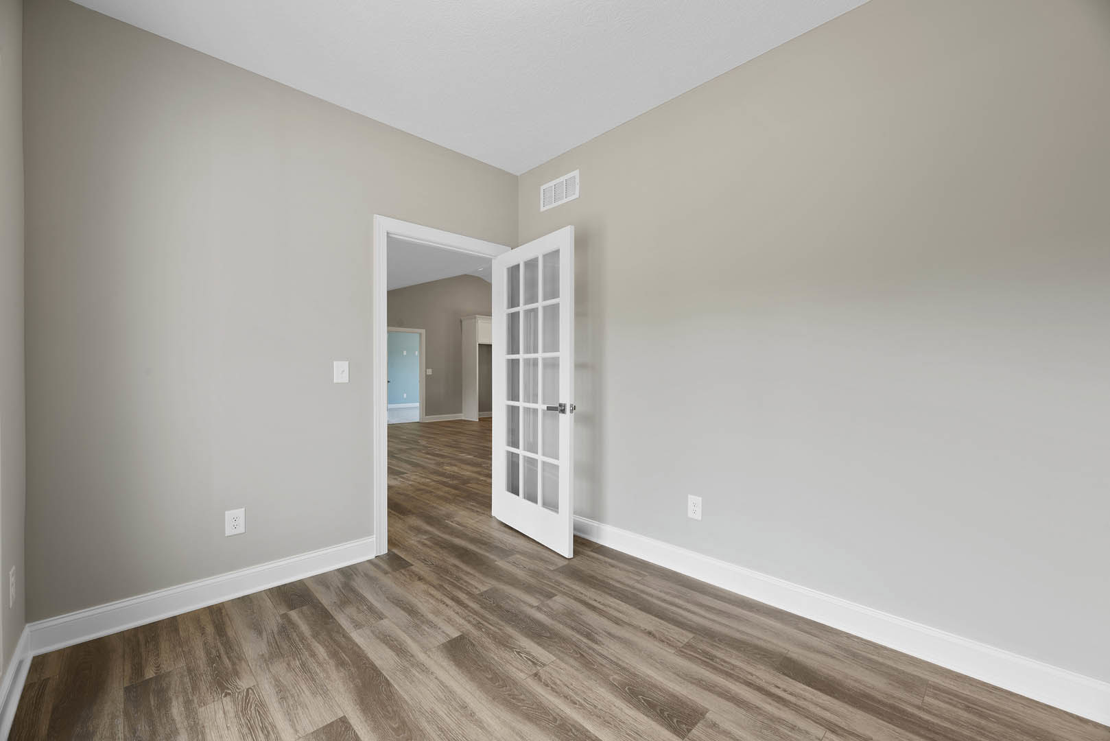 White paneled door with glass panes open to a room with wood laminate flooring, white plaster walls, and a blue accent door; white wall vent visible.