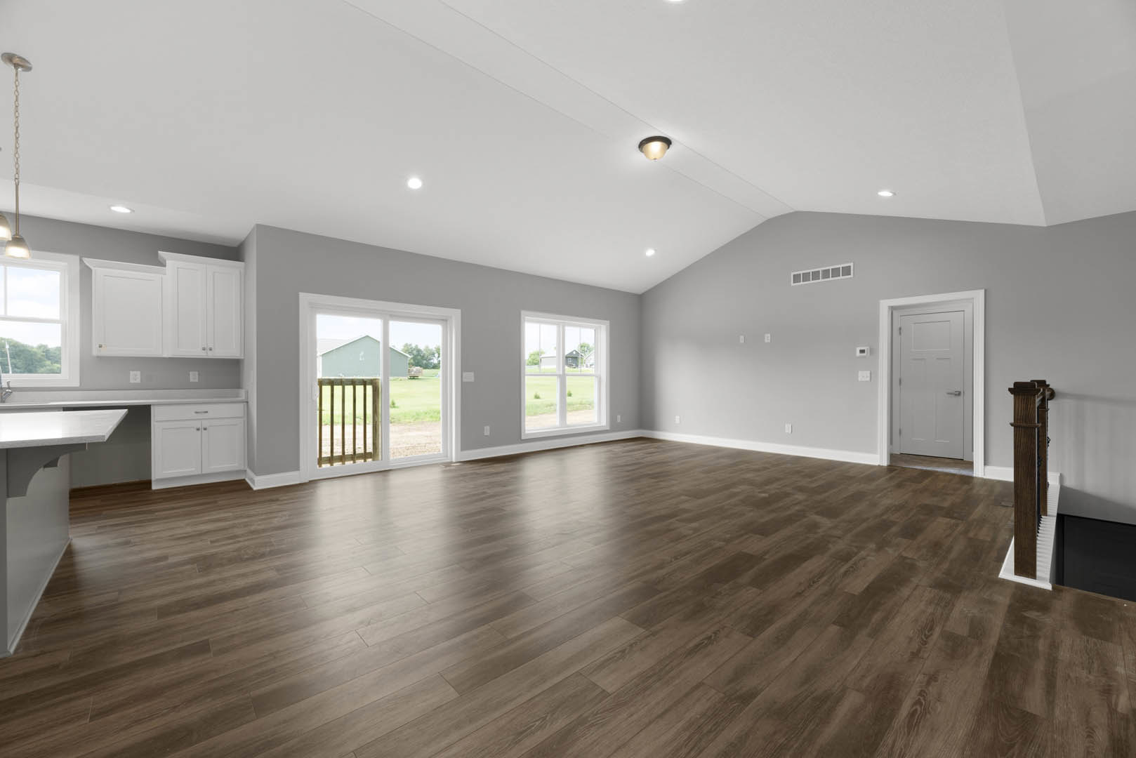 Spacious room with hardwood flooring, white door with silver handle, ceiling light fixture, sliding glass door opening to wooden railing, window overlooking neighboring house