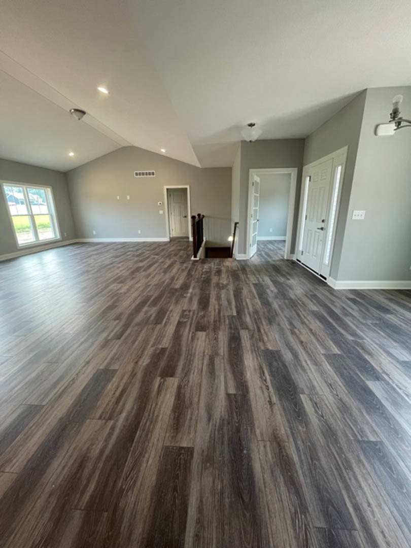 Spacious room with hardwood flooring, white walls, a white door featuring glass panels and black handles, and a window overlooking a grassy field