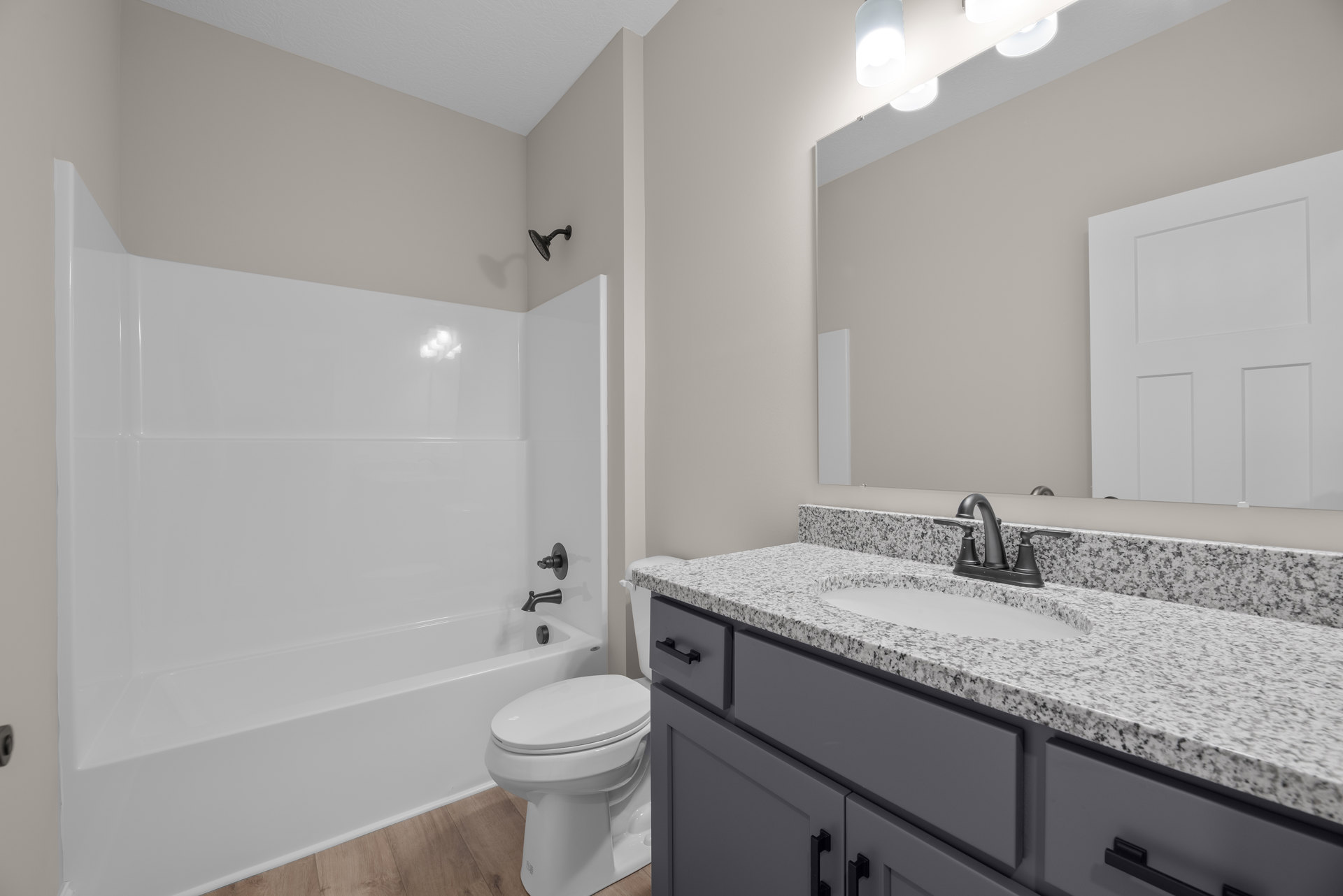 Bathroom with white bathtub, square panel door, wall-mounted shower head, white toilet, sink with cabinetry, and tiled walls.