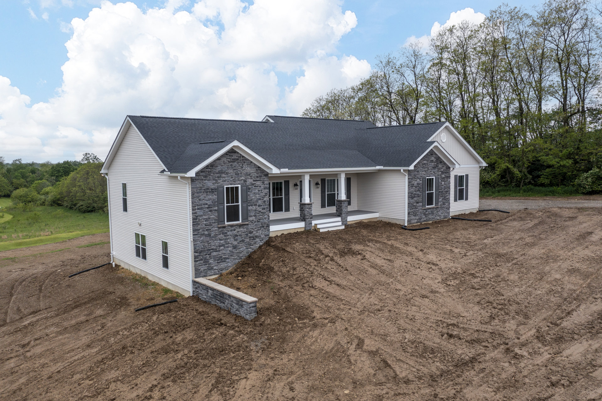 Partially built brick home with exposed glass windows, dirt mound in front yard, and trees visible behind roofline