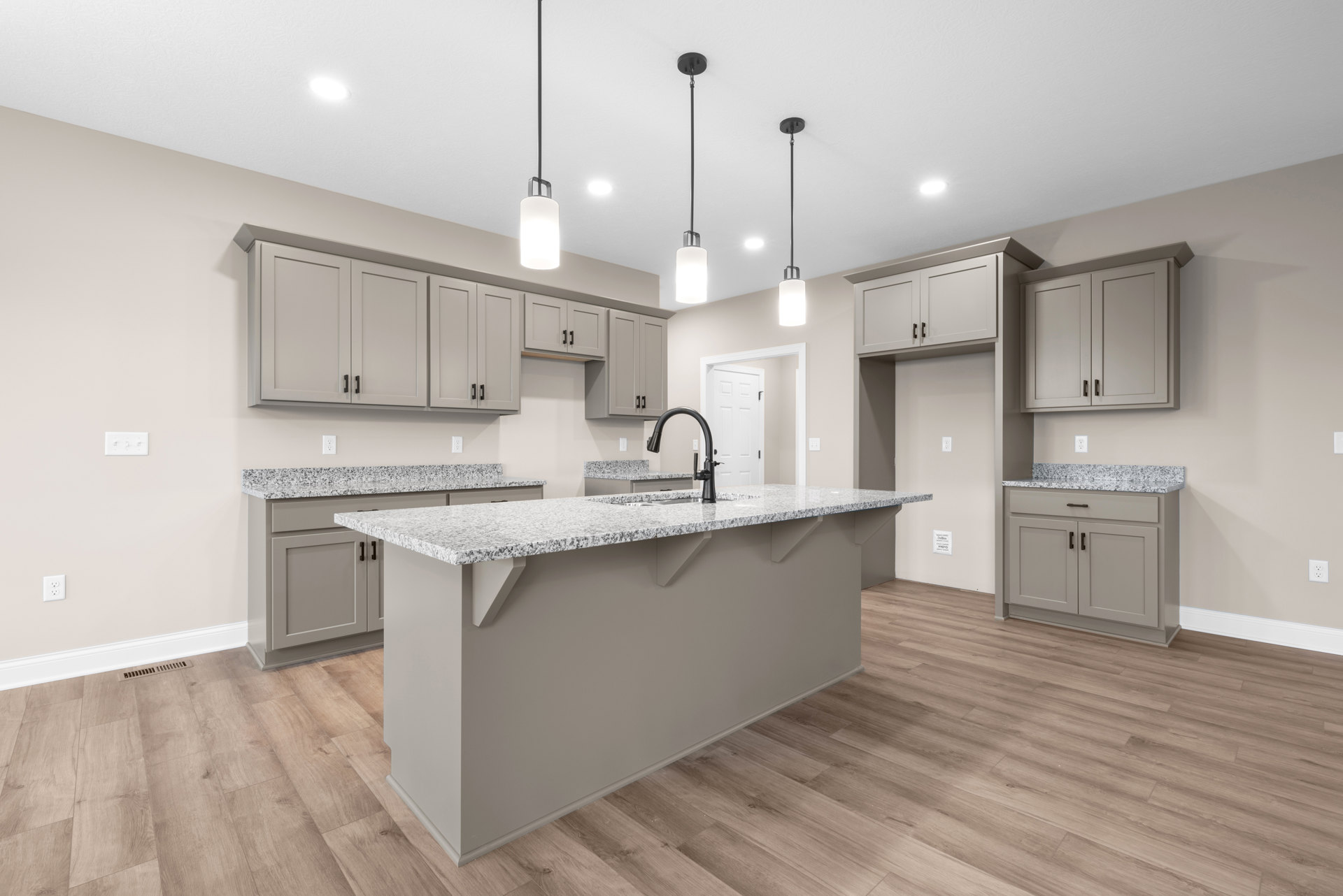 Granite kitchen island with wood flooring, white cabinetry, pendant light fixture, stainless steel sink, and tile backsplash