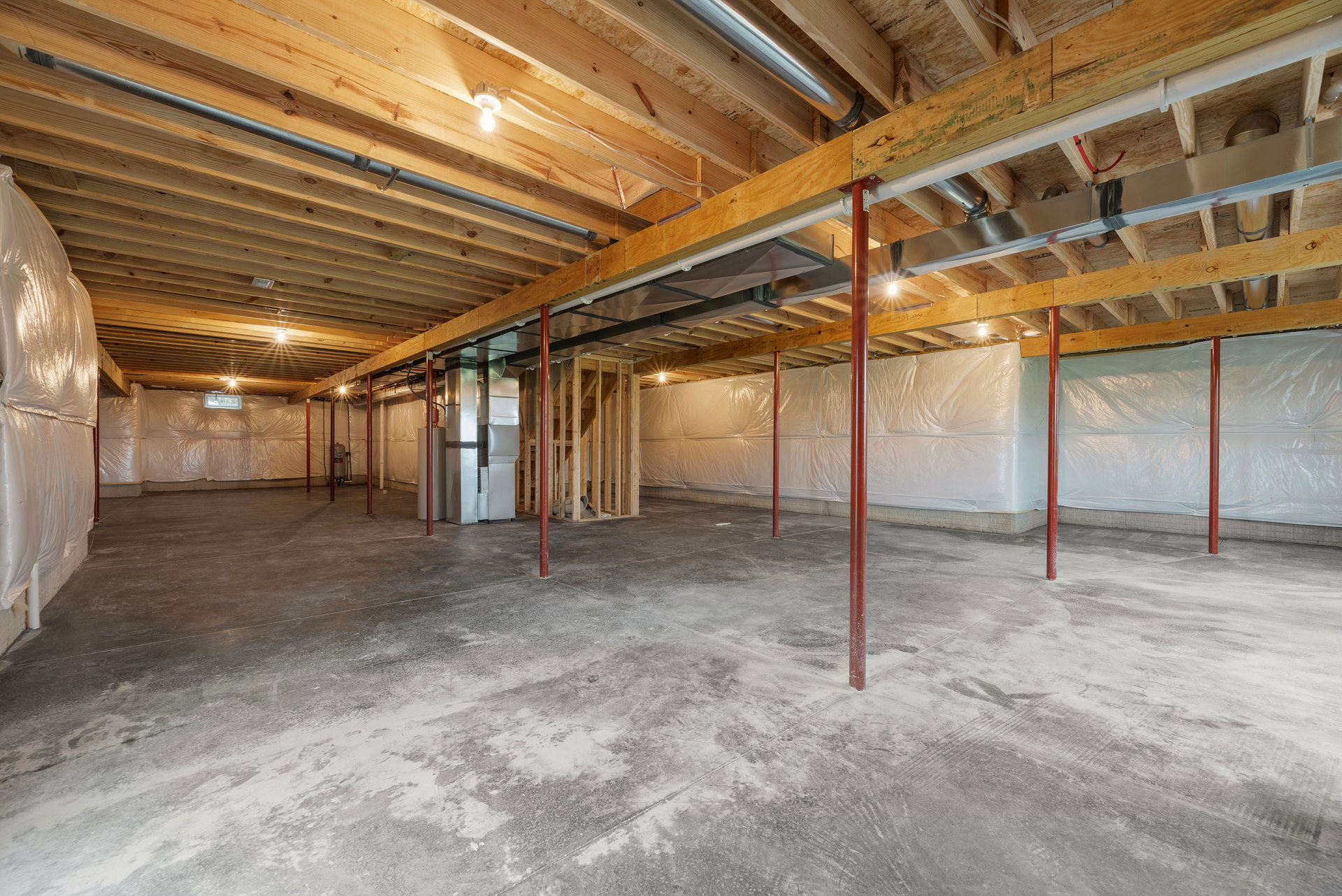 Concrete floor with exposed metal beams and red poles, white plastic bag hanging on unfinished wall in basement interior