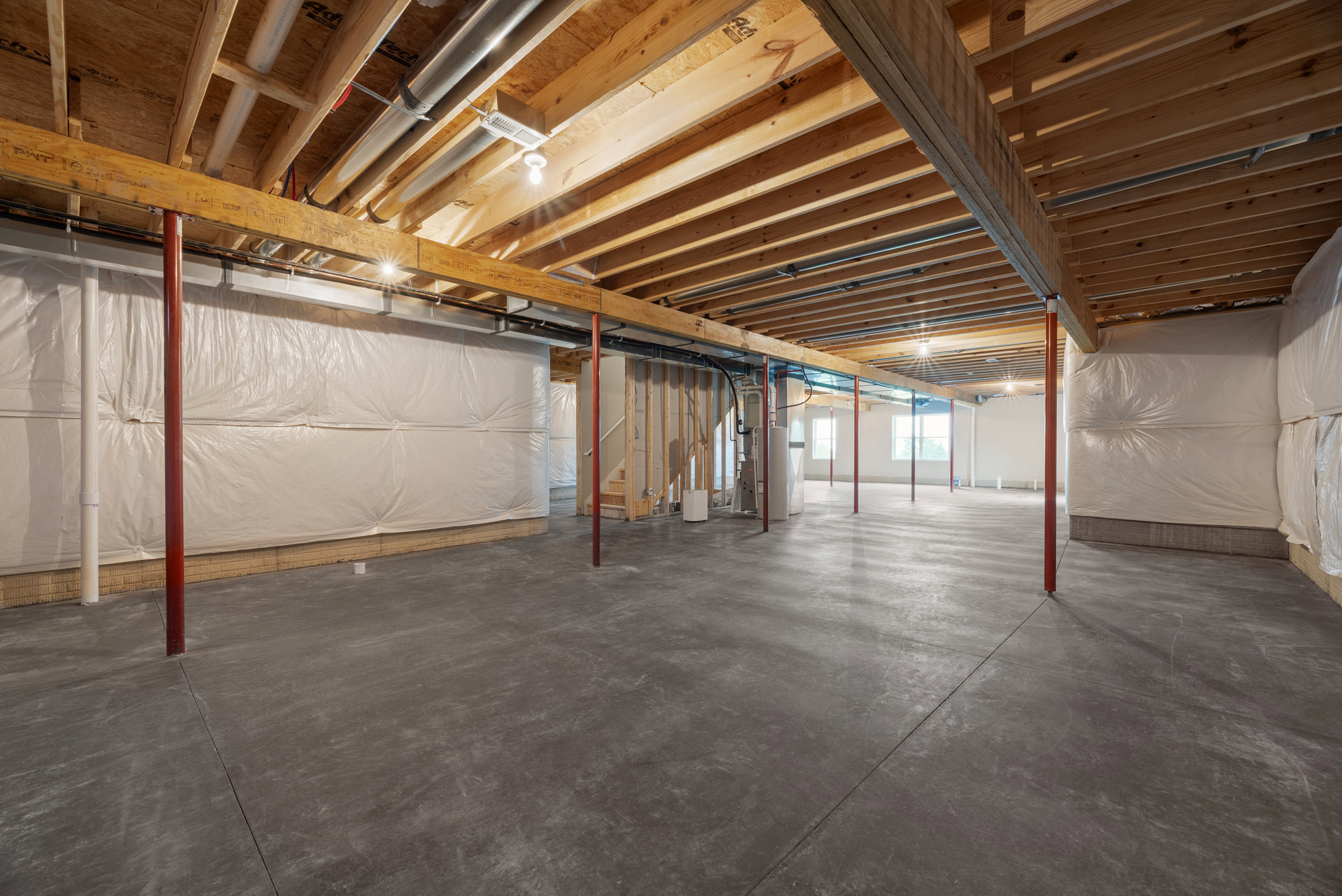 Concrete floor with red support poles, white sheet ceiling, and white walls in an unfinished basement interior