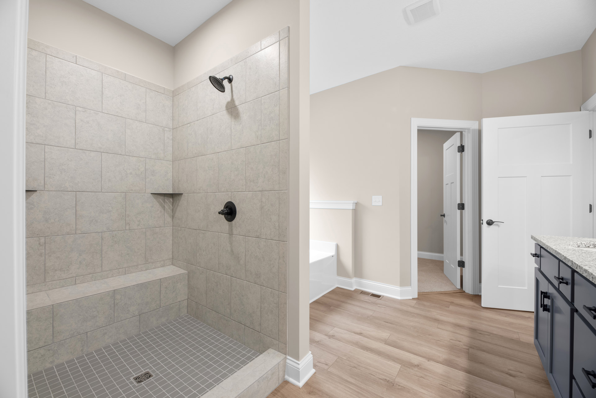 Modern bathroom featuring a walk-in shower with built-in bench, wall-mounted shower head, white tile walls, freestanding bathtub, dark cabinet hardware, and light wood cabinetry