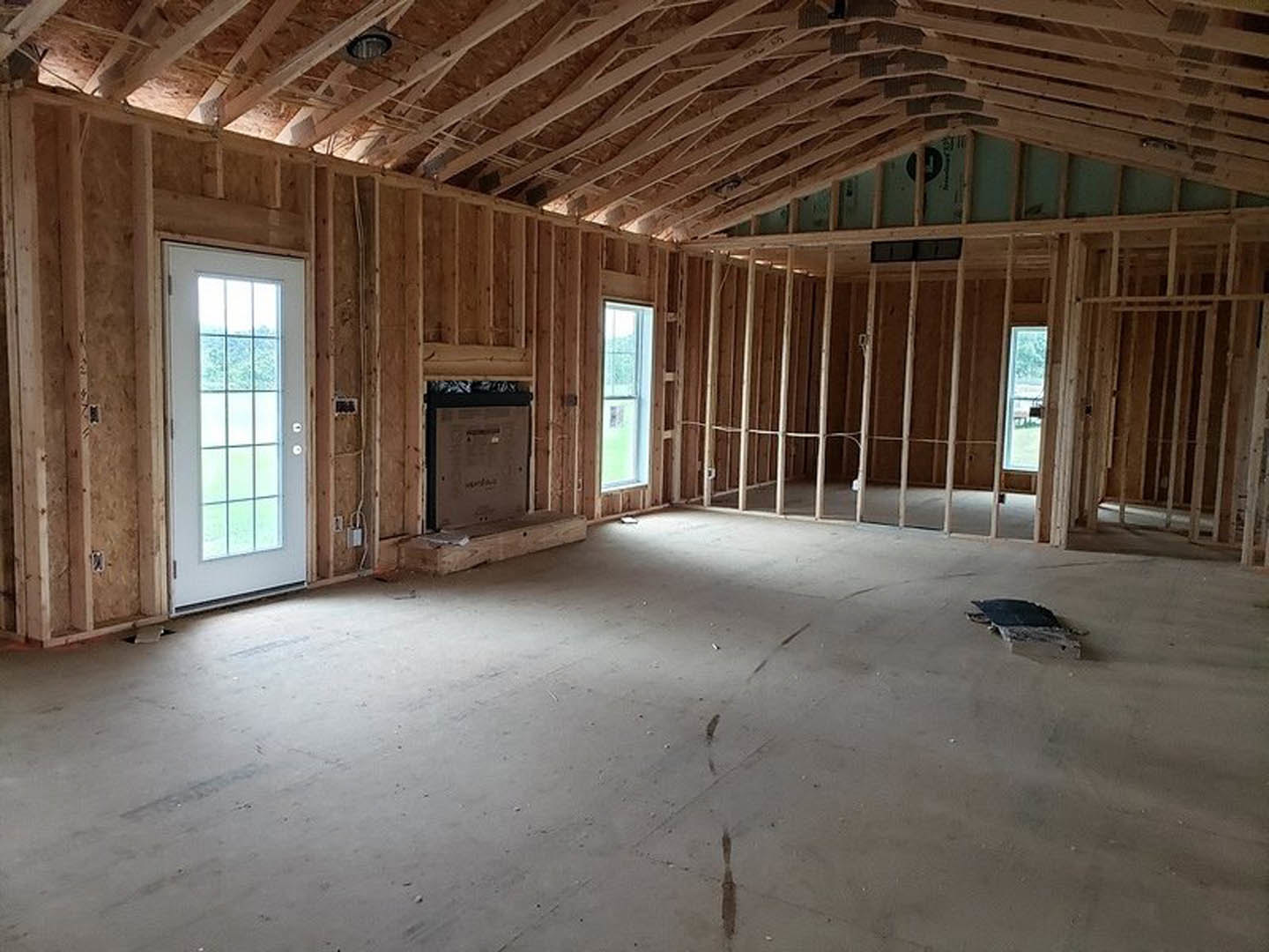 Living room with wood plank ceiling, stone fireplace, white door with glass panes, and hardwood flooring
