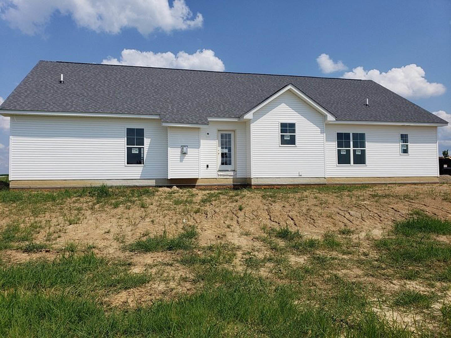 White cottage-style home with multi-pane window, white siding, front door, and patchy grass lawn under a cloudy sky