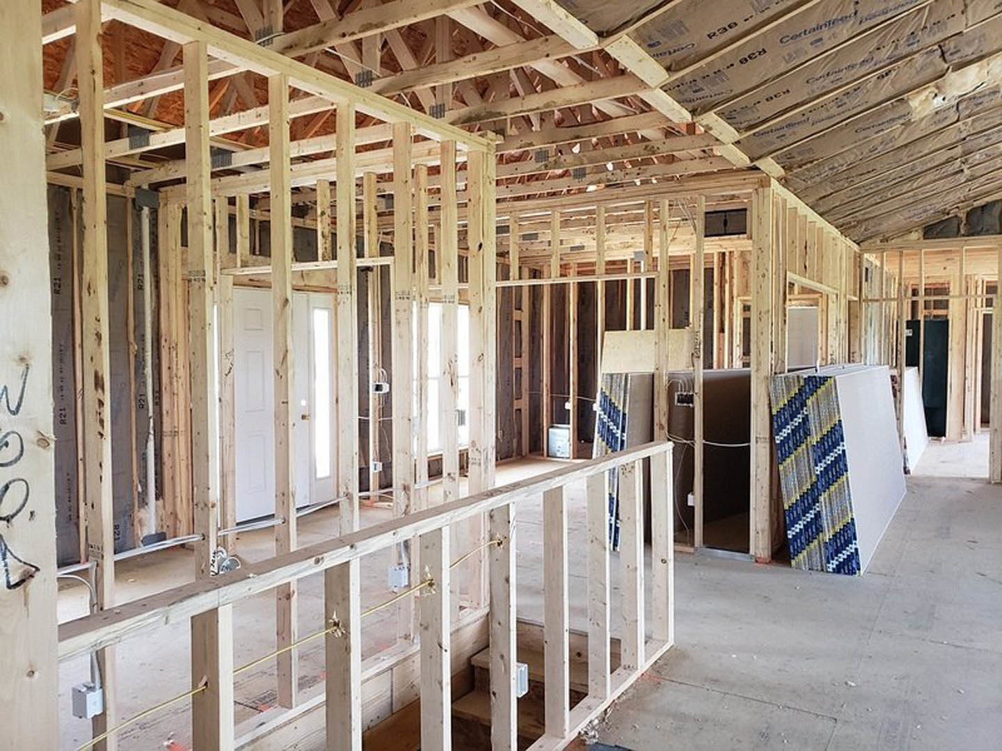 Wood-framed room under construction with exposed beams, unfinished walls, and visible ceiling insulation