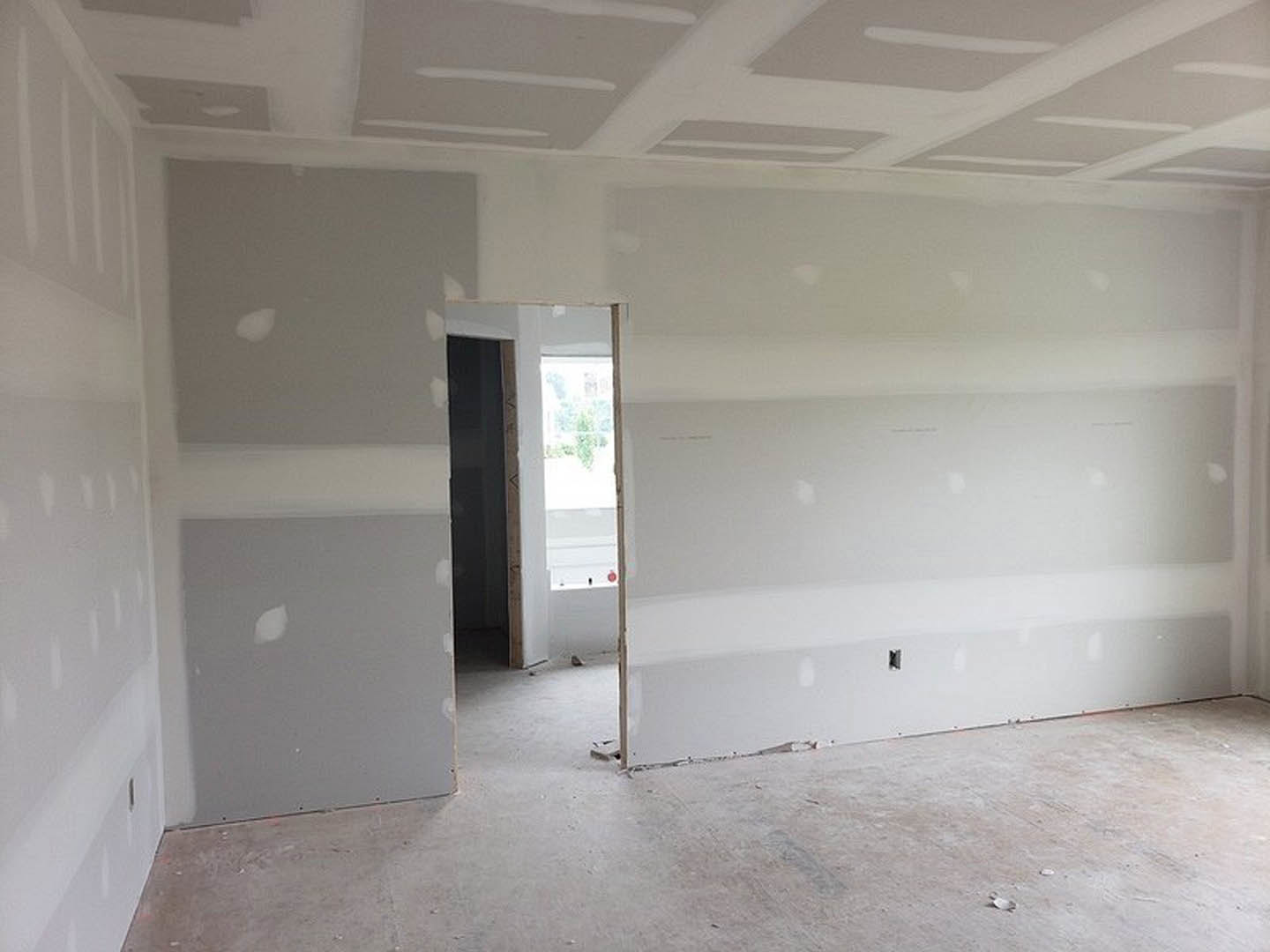 White plaster walls with an open white door, gray flooring, and visible doorway leading to another room