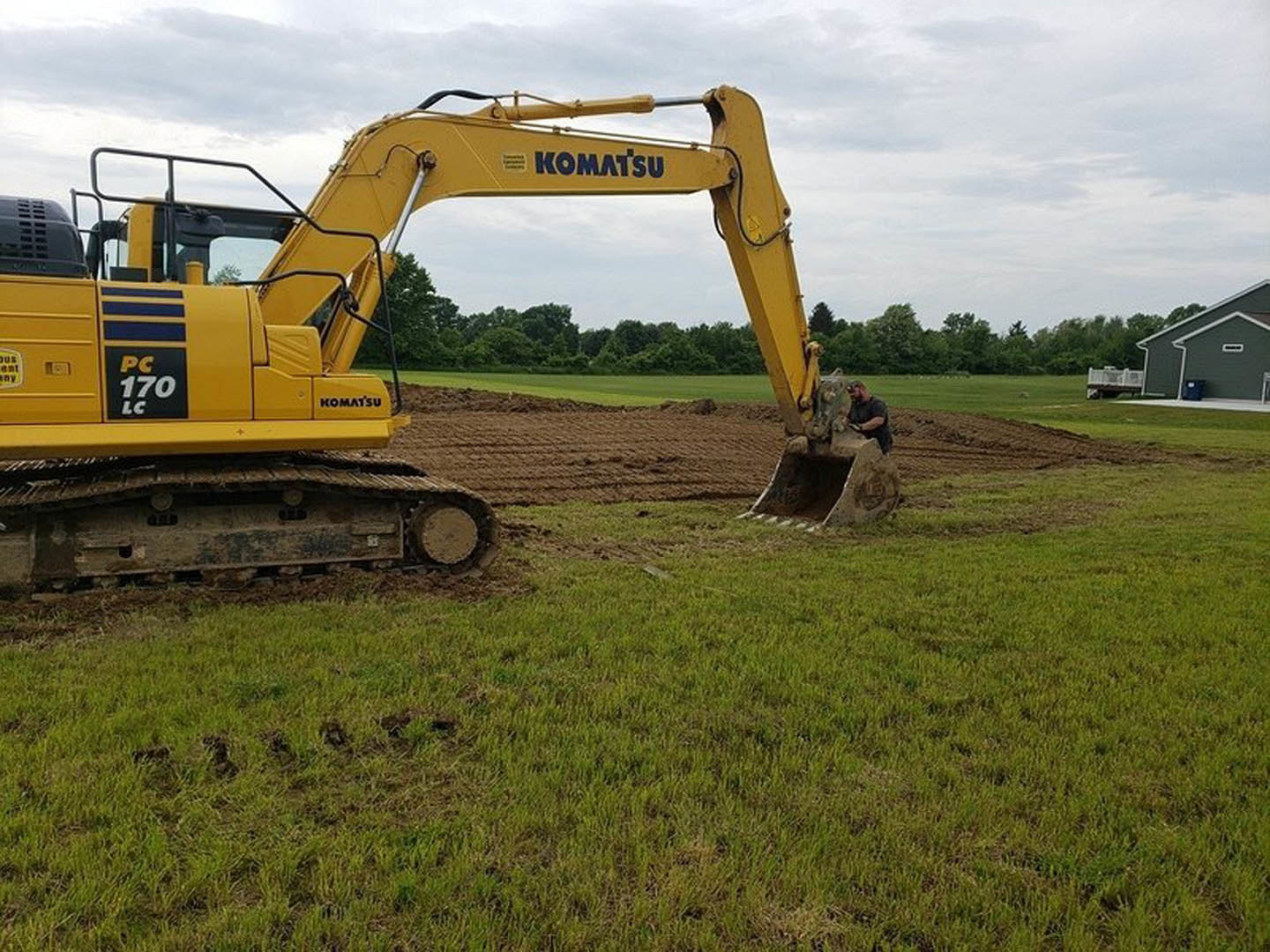 Yellow bulldozer parked on a dirt field with grass and trees in the background, man standing nearby under a clear sky