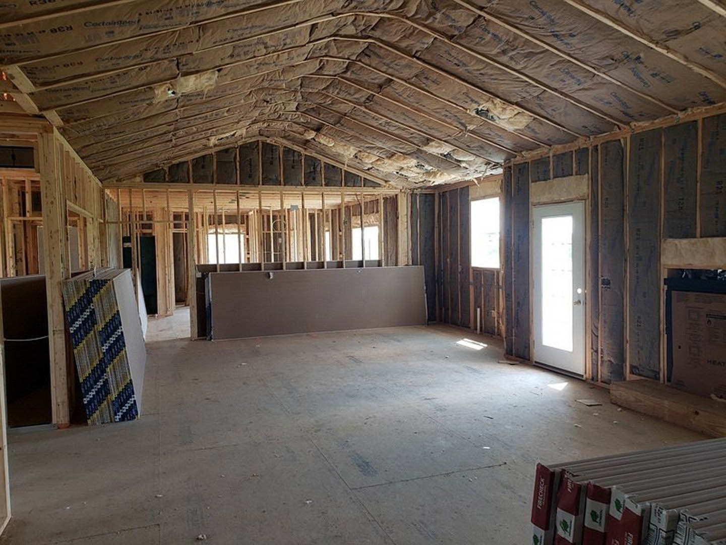 Grey accent wall and white ceiling in a room with a white door letting in natural light, curtain partially visible, stack of boxes on hardwood floor.