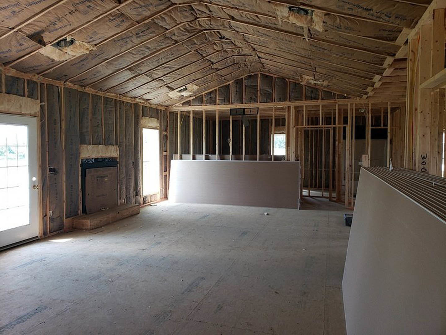 Living room with wood plank ceiling, stone fireplace, large windows, and light streaming onto hardwood floors