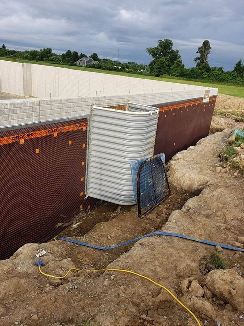 Metal pipe and yellow cable lying in dirt at residential construction site, white container and metal cage nearby, cloudy sky above grassy field.