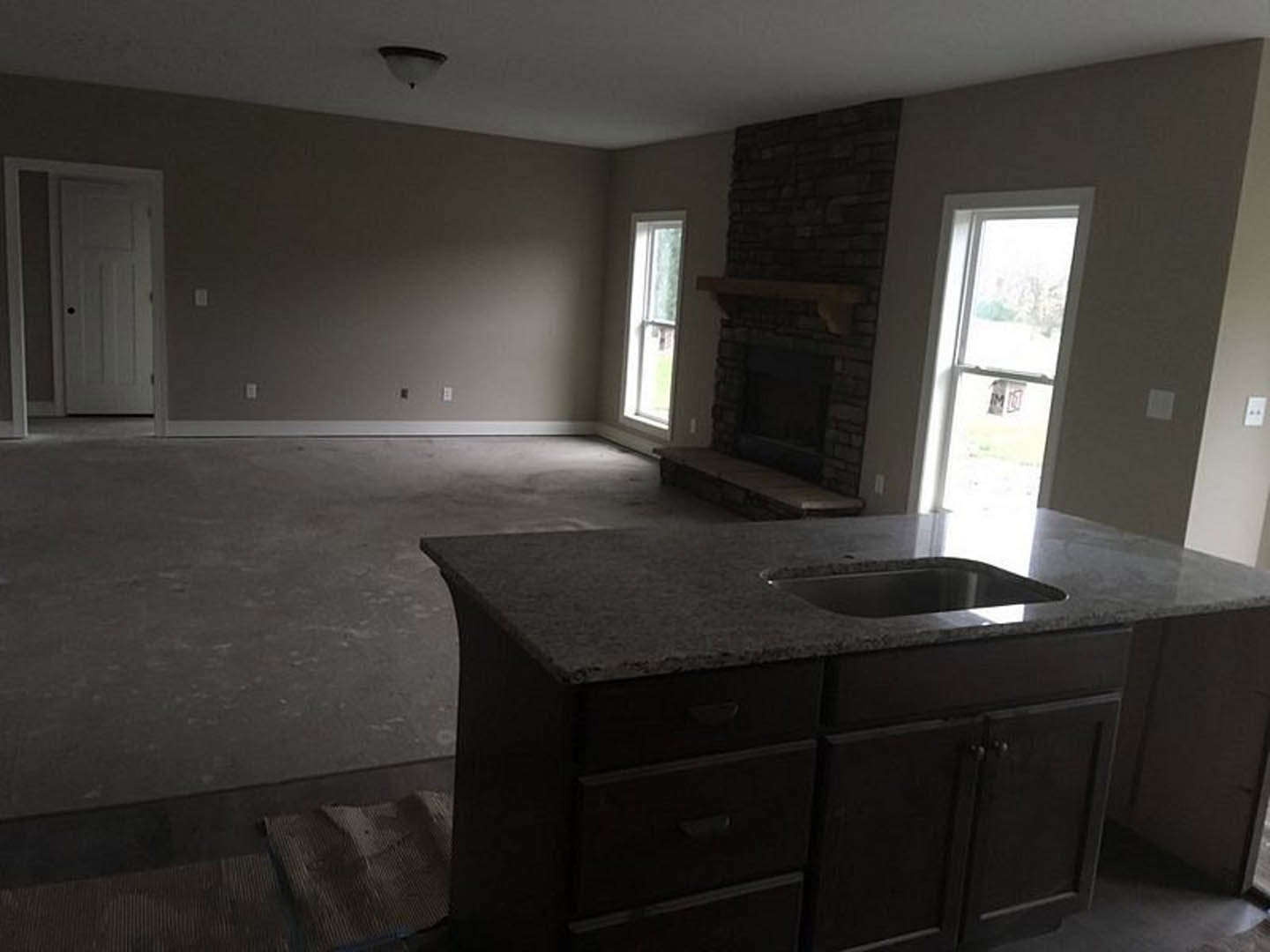 Kitchen with stone fireplace, wood cabinetry, granite countertops, stainless steel sink, pendant lighting, and white door leading to adjacent room