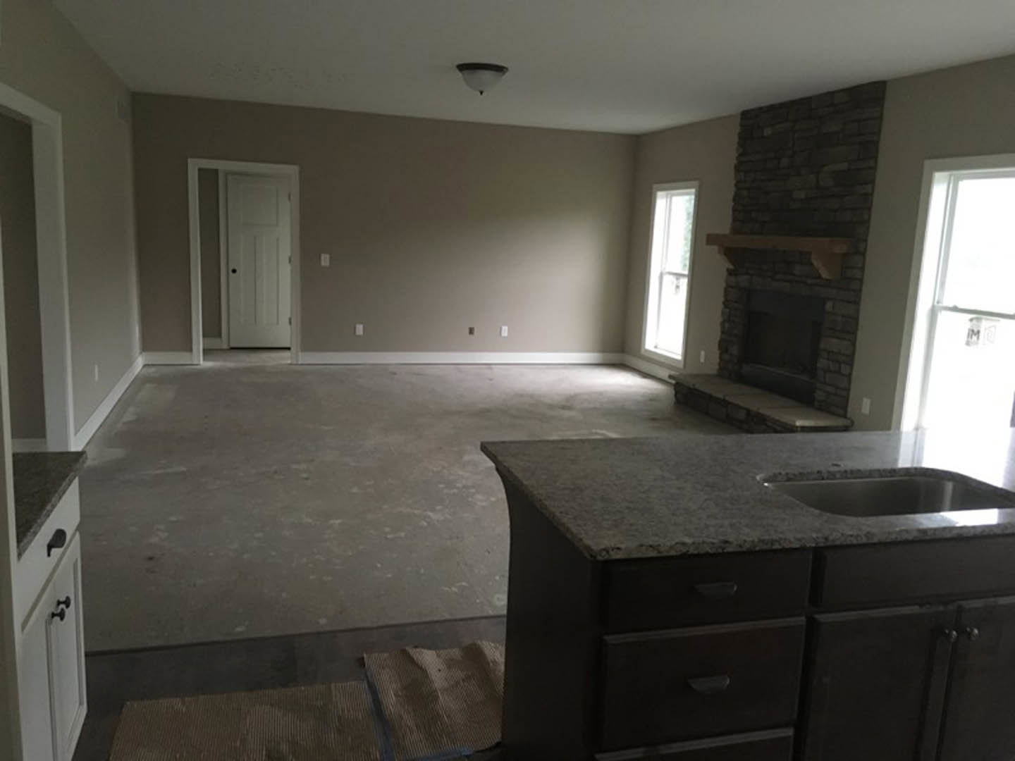 Open-concept kitchen and living room featuring a stone fireplace, white cabinetry, quartz countertop with undermount sink, hardwood flooring, recessed lighting, and large windows