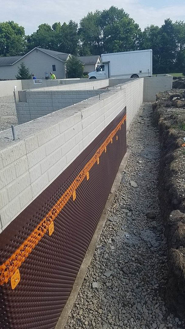 Brick exterior wall with brown and orange plastic sheeting, white truck parked nearby with door open, concrete wall close-up, group of people standing outside, rocky landscaping