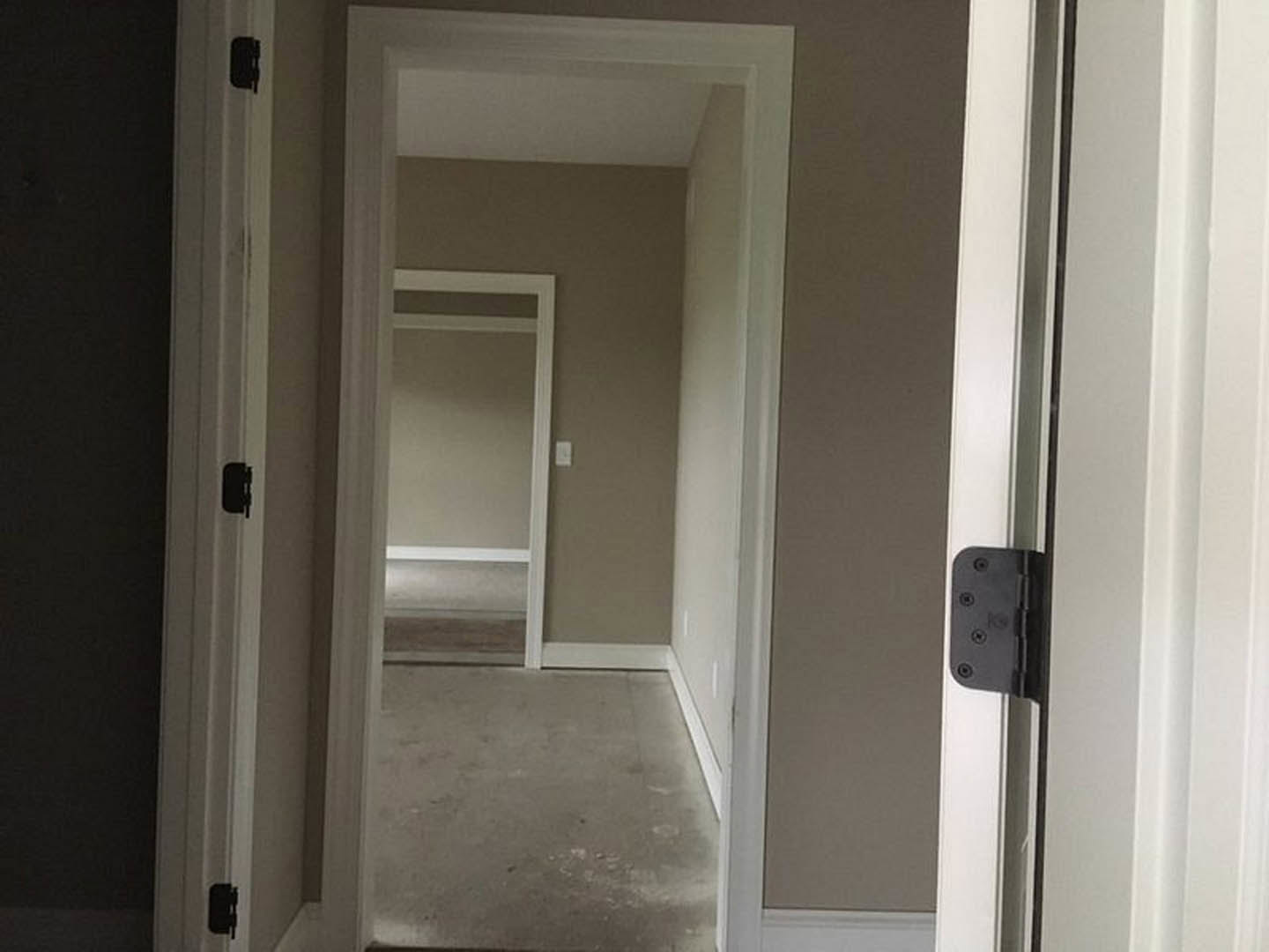 White hallway with open door, black hinge and handle, white plaster walls, white door frame, grey concrete floor with white base trim