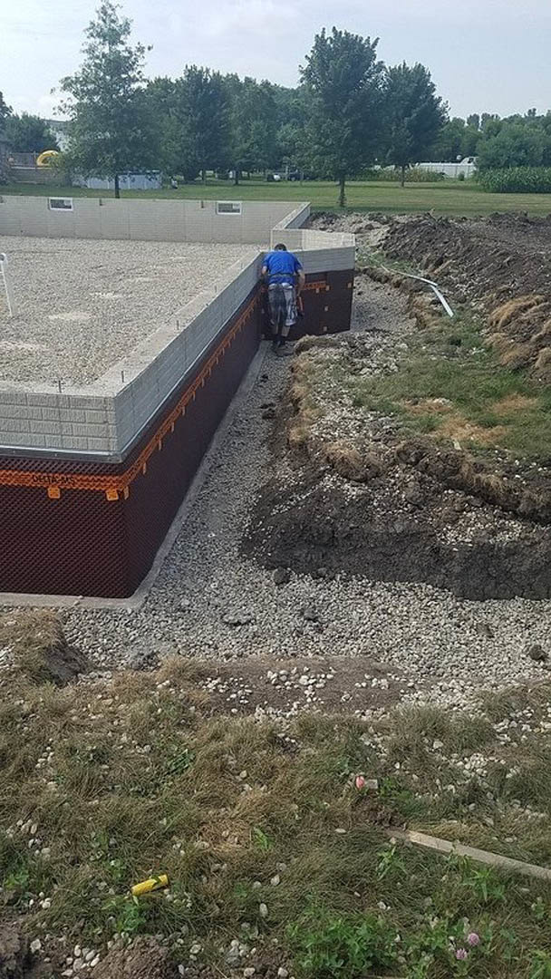 Modern home exterior with light stone walls, expansive lawn, mature trees, and a man standing on a low garden wall under a clear sky
