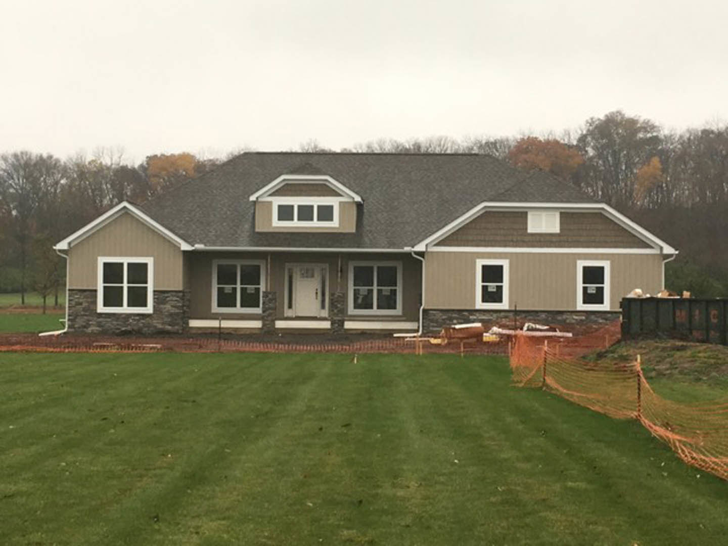 Two-story house with white siding, black-trimmed windows, white front door, covered porch, manicured green lawn, wooden fence, and mature trees under a clear sky