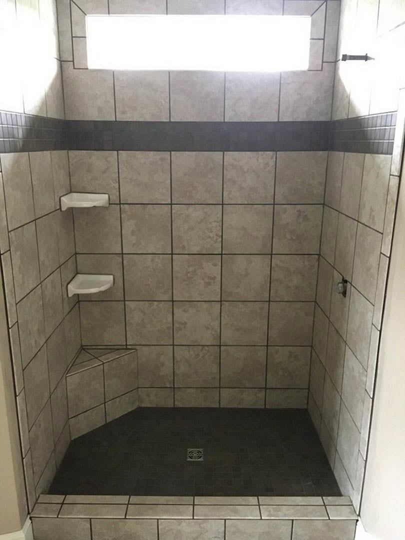 Walk-in shower with white tiled walls, glass door, and recessed ceiling light illuminating the space