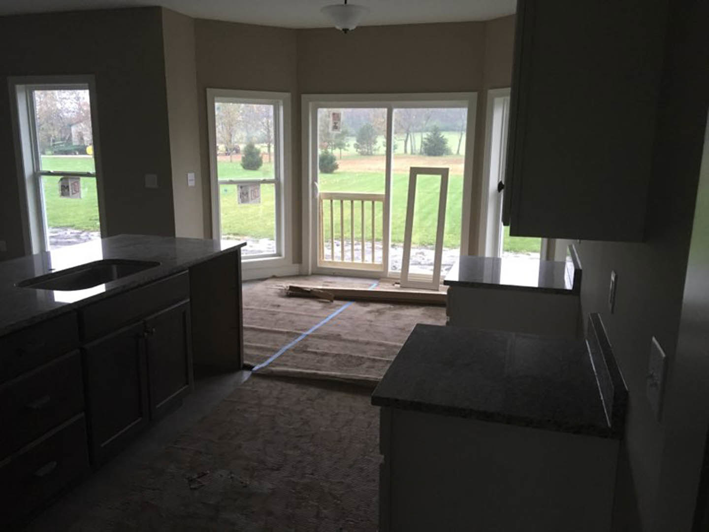 Modern kitchen with light wood cabinetry, stainless steel sink, open door leading to balcony, large window, and hardwood flooring
