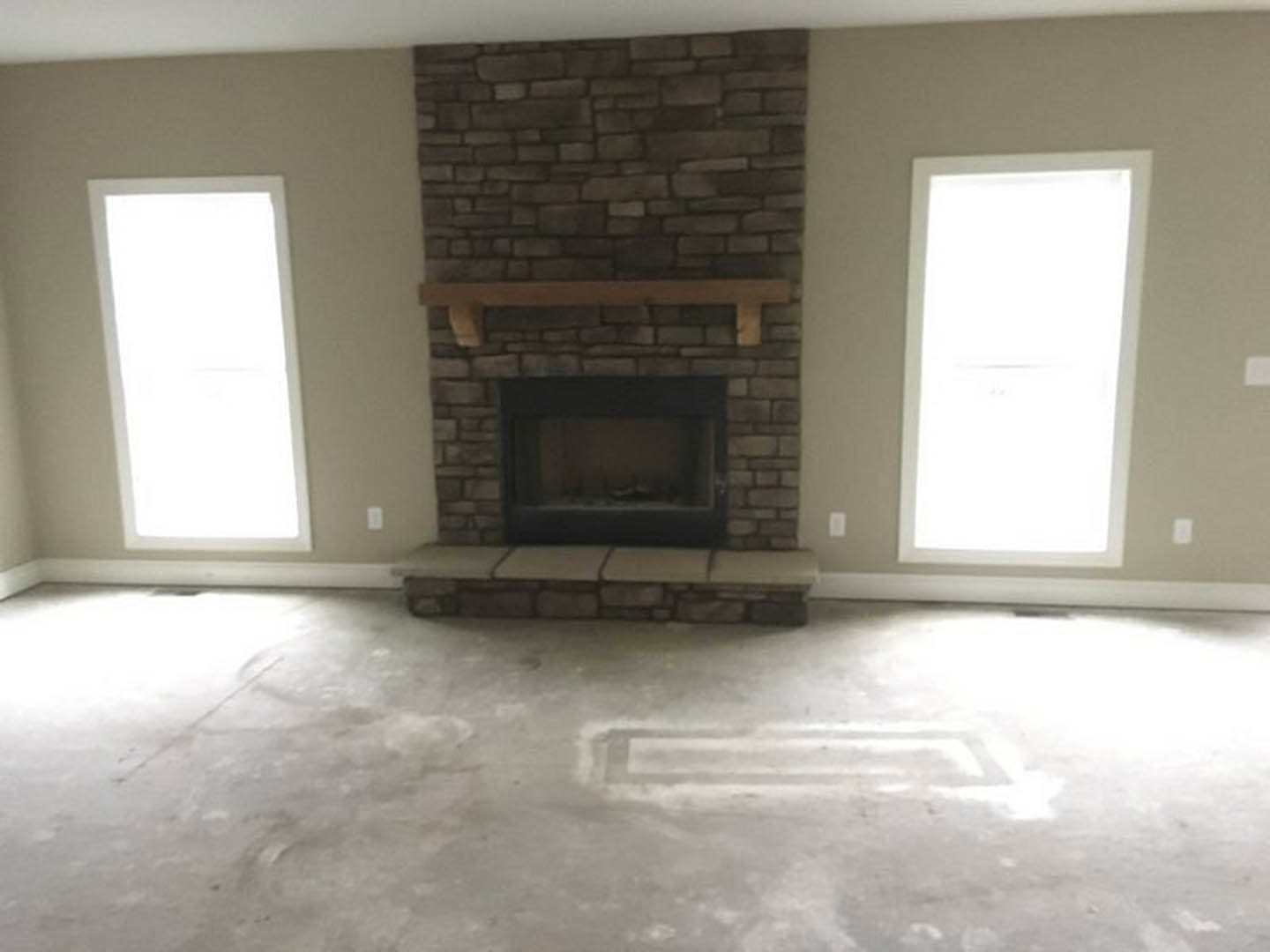 Brick fireplace with wooden mantel, white rectangular window letting in natural light, concrete floor with square pattern, plaster walls in a modern living room.