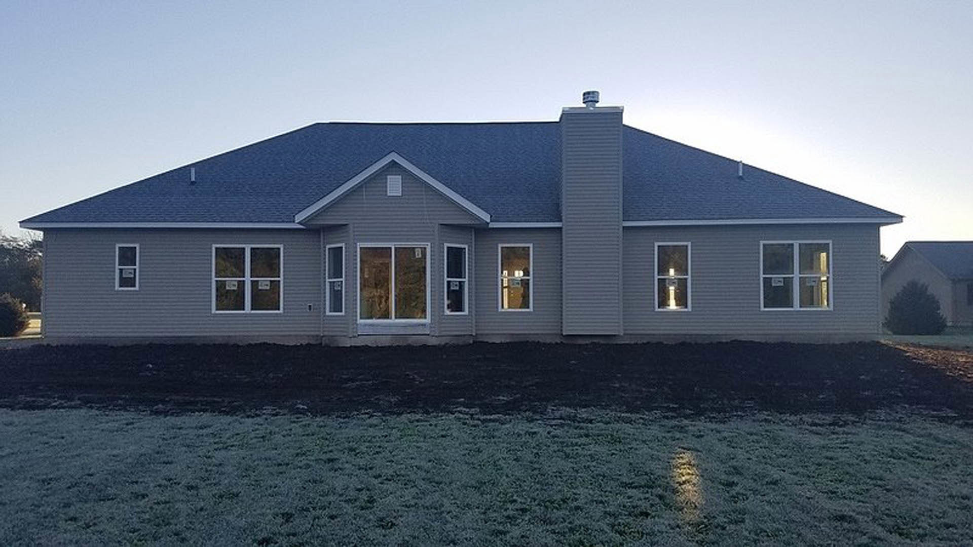 Two-story house with blue roof, white siding, illuminated windows, and green lawn in front