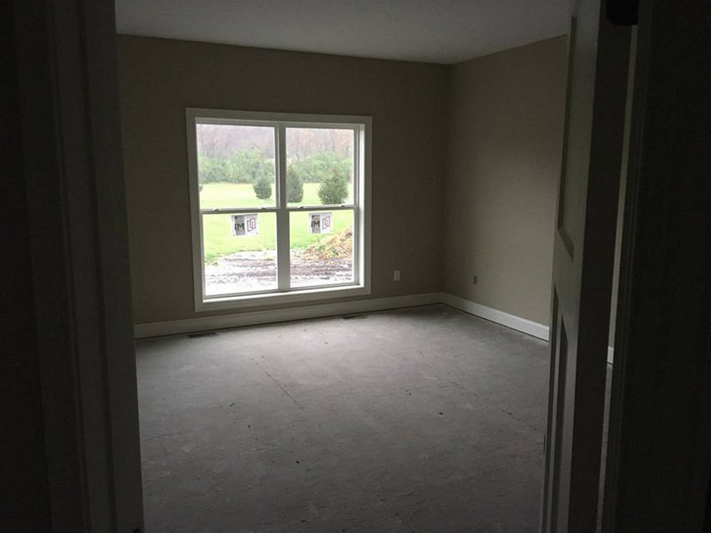 Concrete floor and white walls with black trim, large window overlooking grassy field, close-up of door and blurred logo in foreground.