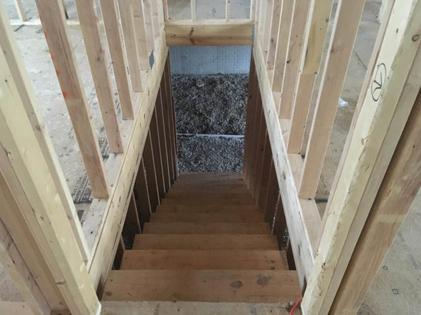 Wooden staircase with matching handrail, white brick accent wall, large window framed in wood, black house number on white surface, brown plank flooring