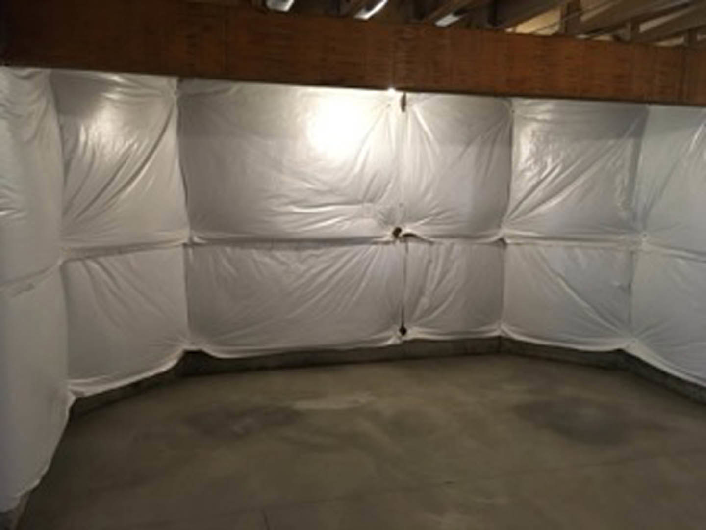 Room with white plastic coverings draped over walls and floor, white ceiling, and neutral-toned surfaces visible.