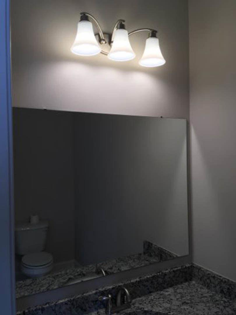Modern bathroom with white plaster walls, rectangular mirror above a sleek sink, chrome faucet, and contemporary light fixture mounted on the ceiling