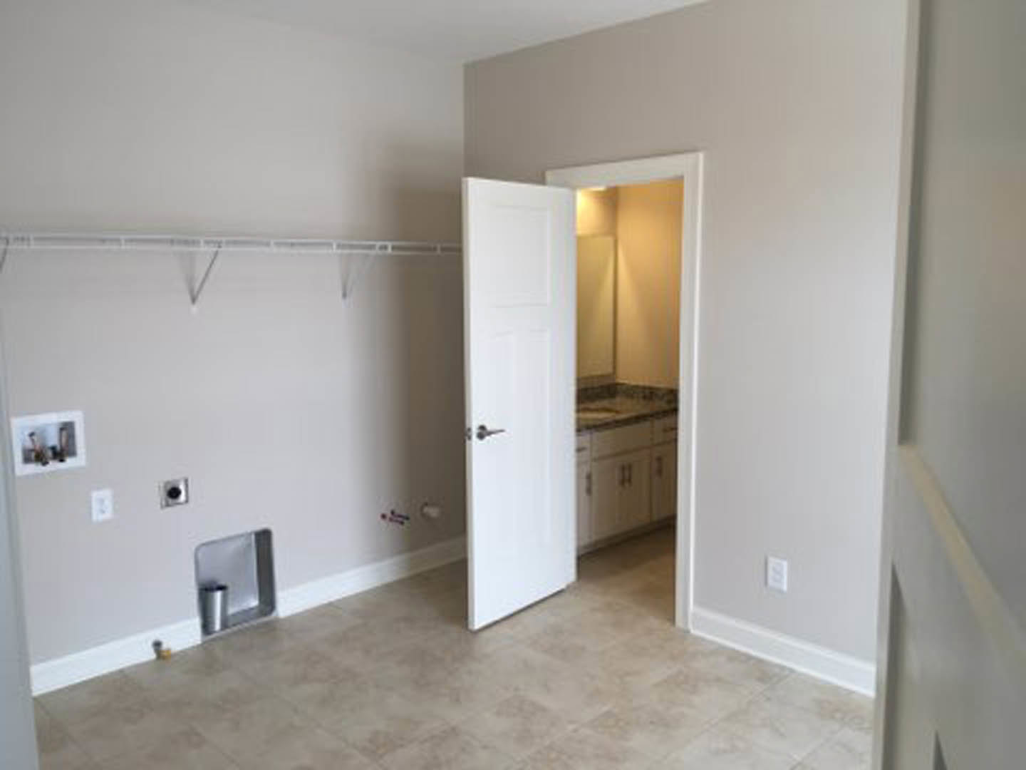 White bathroom with open door, wall-mounted sink, light tile flooring, plaster walls, and minimalist cabinetry