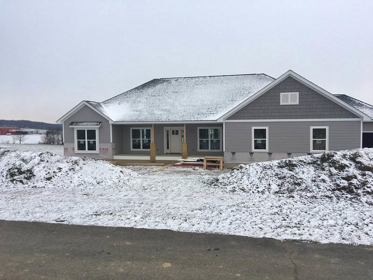 Two-story house with white siding, snow covering the roof and ground, white-framed windows, and a close-up view of the front door.