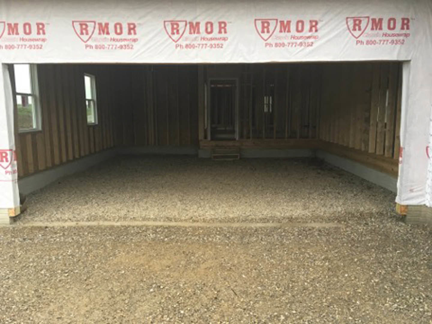 Framed residential structure under construction with exposed plywood, visible window opening, and white construction banner attached to exterior wall