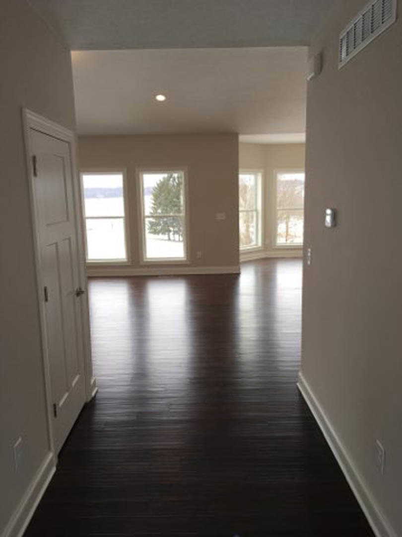 Dark hardwood flooring, white walls, white door with silver handle, ceiling vent, large windows with view of leafy trees