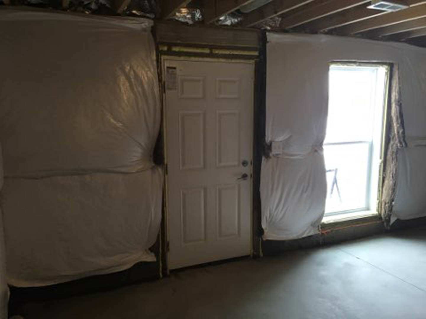 White-painted bedroom with a white door featuring a black handle, white leather couch, window dressed with sheer white curtain, light-colored walls and flooring