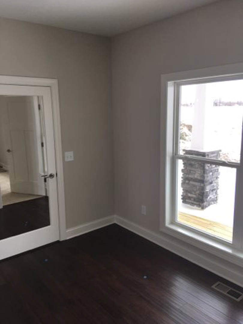 Dark wood flooring with white baseboard trim, stone pillar detail, white door featuring a silver handle, large window letting in natural light, plaster walls